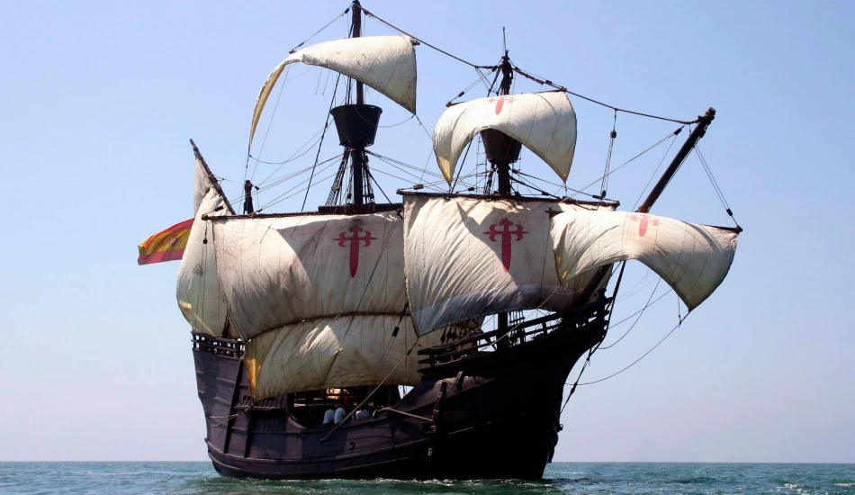 A replica of a historic Spanish carrack sailing on the sea with cream-colored sails and red crosses.
