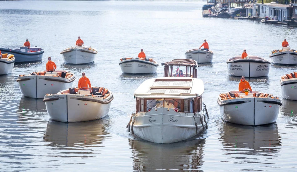 A group of boats with passengers in orange jackets navigating a sunlit waterway.