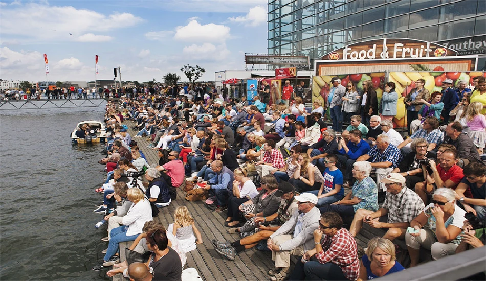 Tourists and locals seated at a pier watching the Sail Amsterdam waterfront activities.