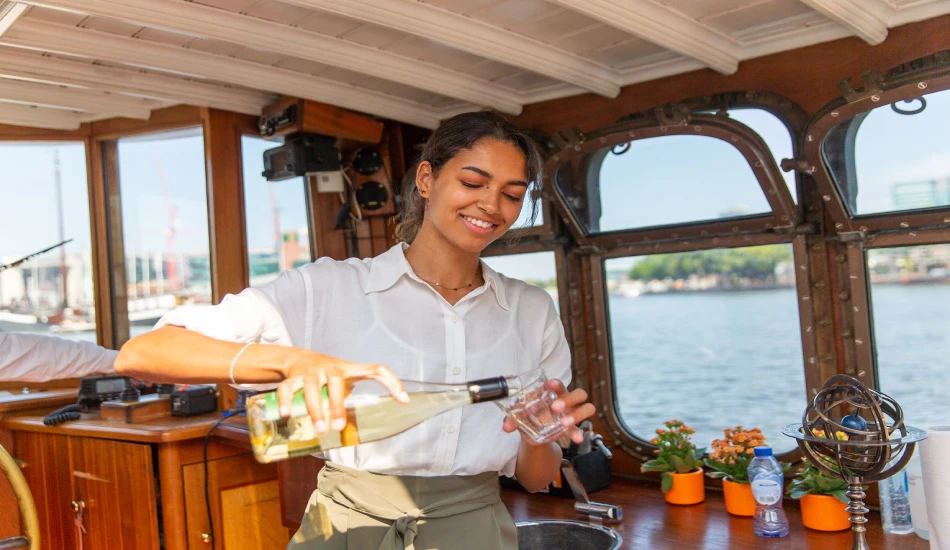 A women is pouring drink in a glass in a boat.