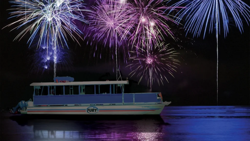 Fireworks in background of a boat A boat named "Fury" floats on water, illuminated by vibrant fireworks.
