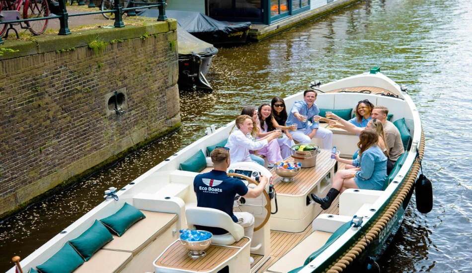 A group of people enjoy a festive gathering on a boat, raising drinks and sharing laughter along a picturesque canal.