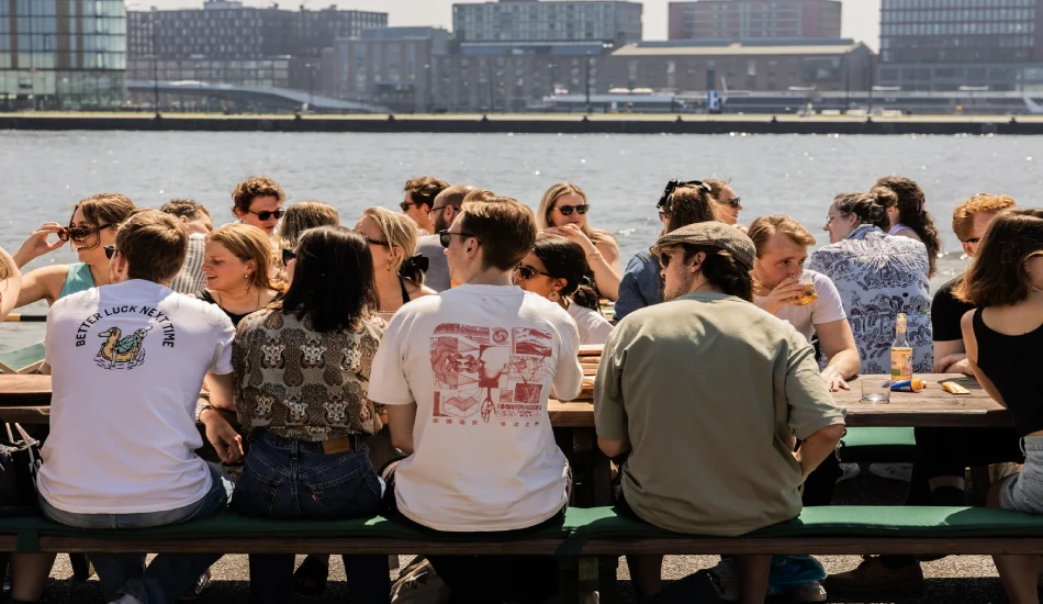 Casual waterfront meal with groups of people eating, drinking, and chatting.