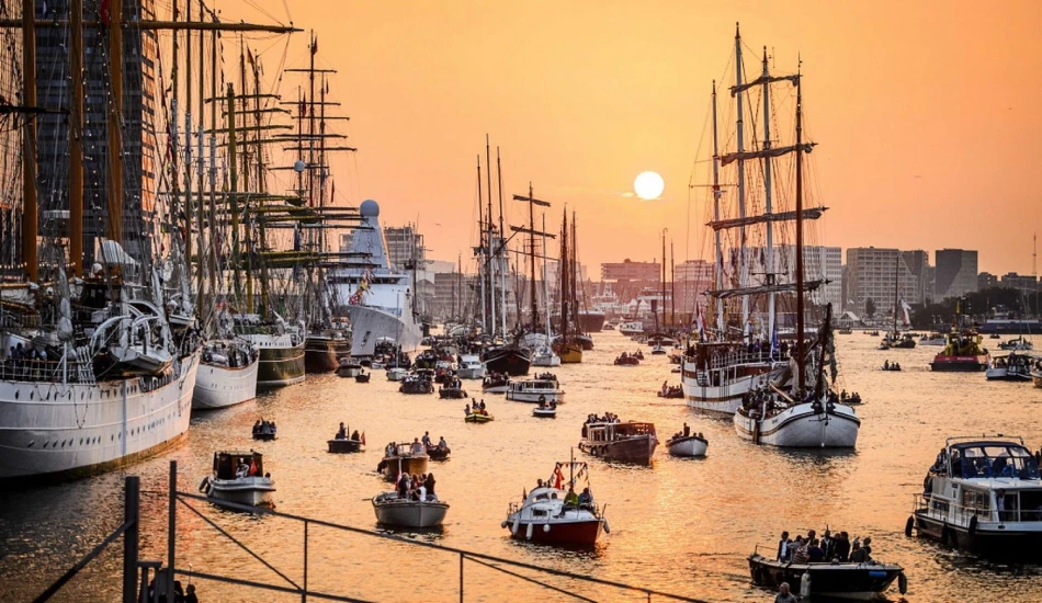 reasons-for-visiting-sail-amsterdam Sunset over a packed Amsterdam harbor filled with sailboats and historical ships.