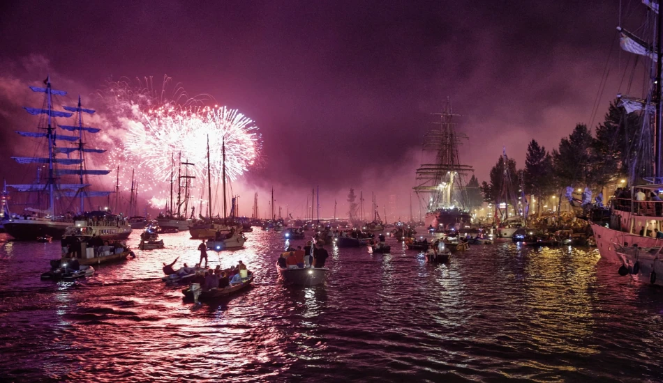 A nighttime scene of a harbor with fireworks, illuminated ships, and small boats.