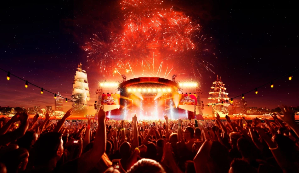 Fireworks light up the night sky at a Sail Amsterdam concert with ships in the background.