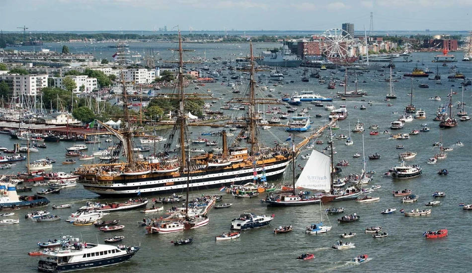 A huge number of tall ships and boats sailing in the river.