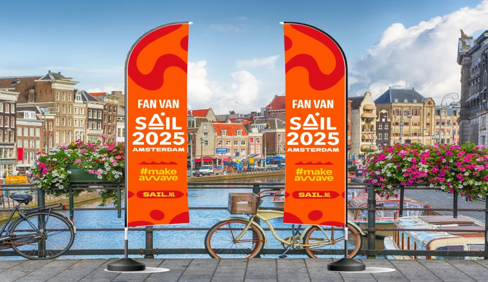 Two colorful flags promote SAIL 2025 in Amsterdam against a scenic canal backdrop.