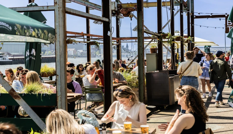 A lively outdoor café scene by the water, filled with people dining and enjoying drinks.