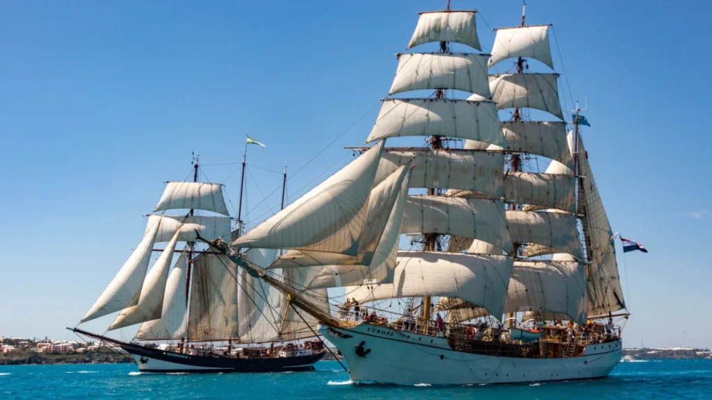 Tall sailing ships with full white sails on blue ocean water during a maritime festival.