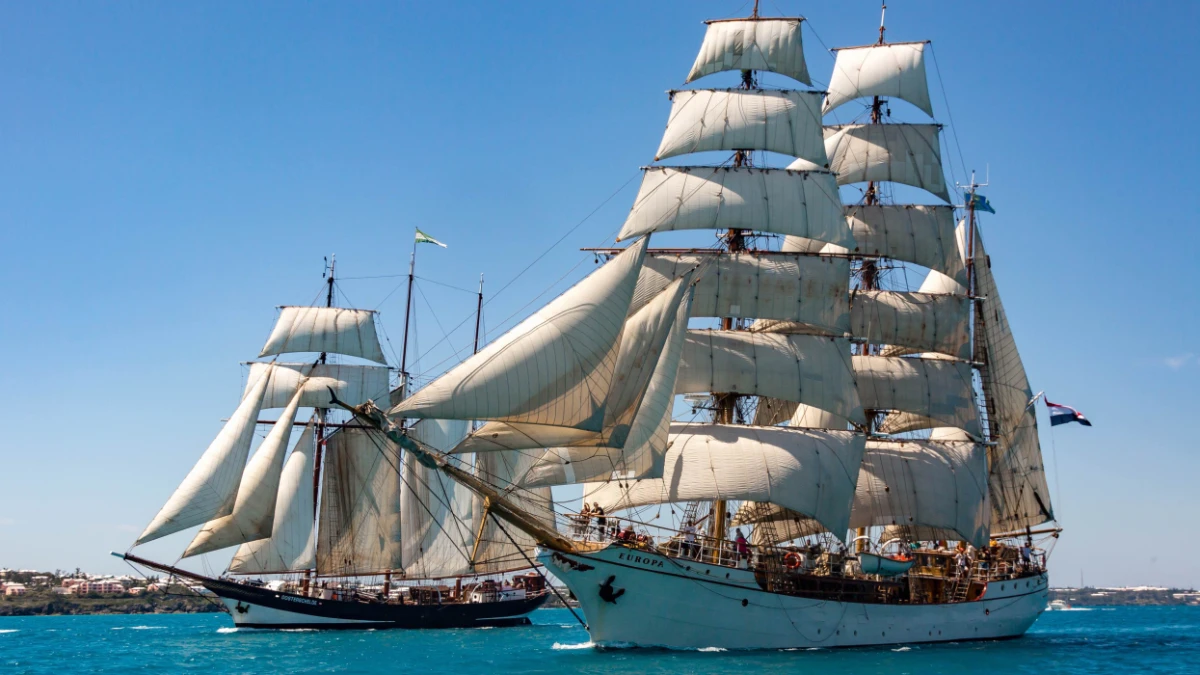 Tall sailing ships with full white sails on blue ocean water during a maritime festival.
